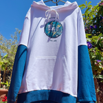 White and blue hoodie with a logo on a stand against a natural background